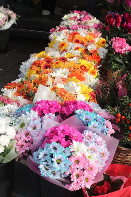 A collection of vibrant flower bouquets arranged on a display table, featuring a variety of fresh flowers including pink, white, orange, and yellow blossoms. The bouquets are wrapped in pastel and whi
